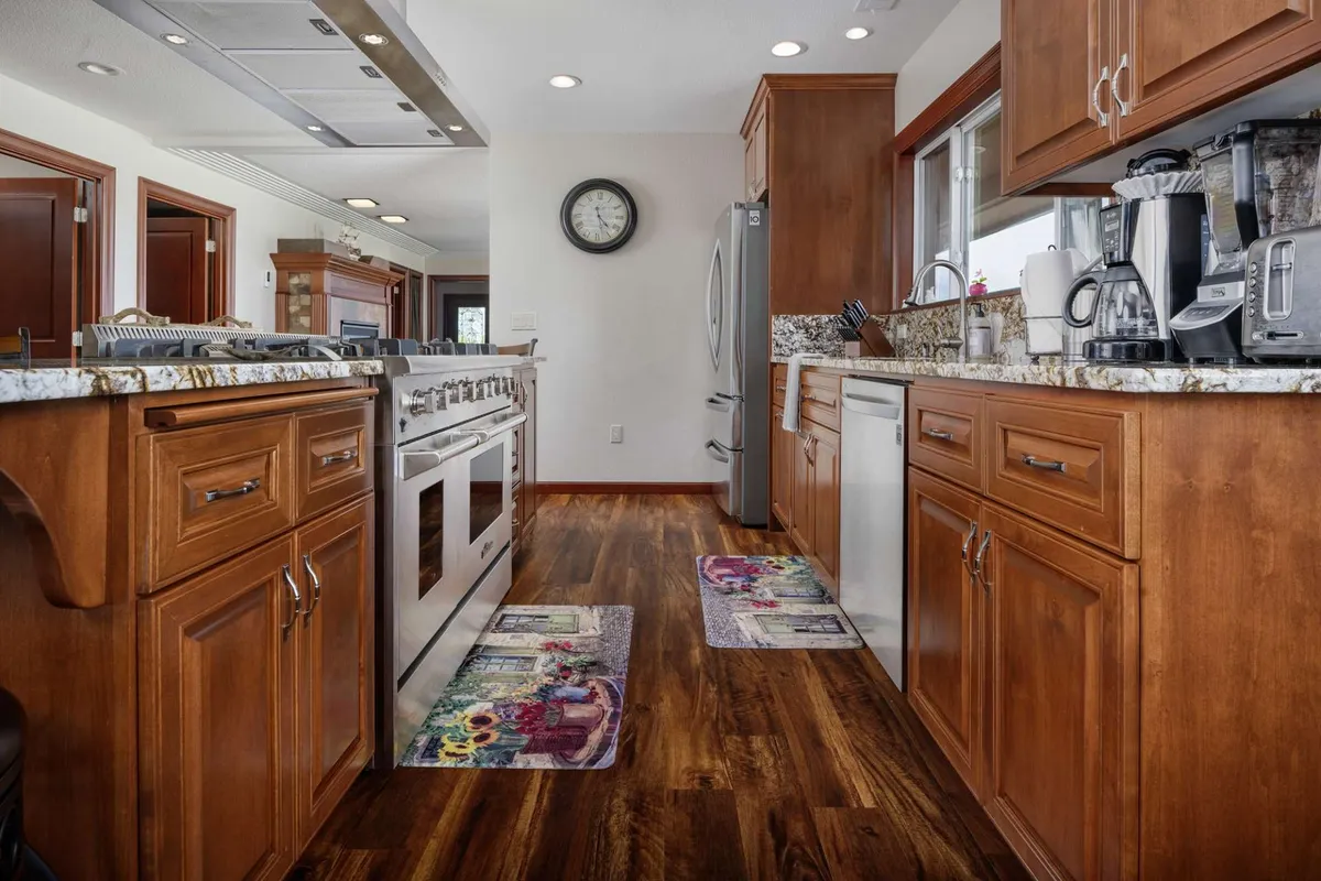 A warm, inviting kitchen space featuring granite countertops, stainless steel appliances, wooden cabinetry, and colorful rugs. The kitchen is set up for cooking, meal preparation, and entertaining guests, with ample countertop space and premium appliances visible.
