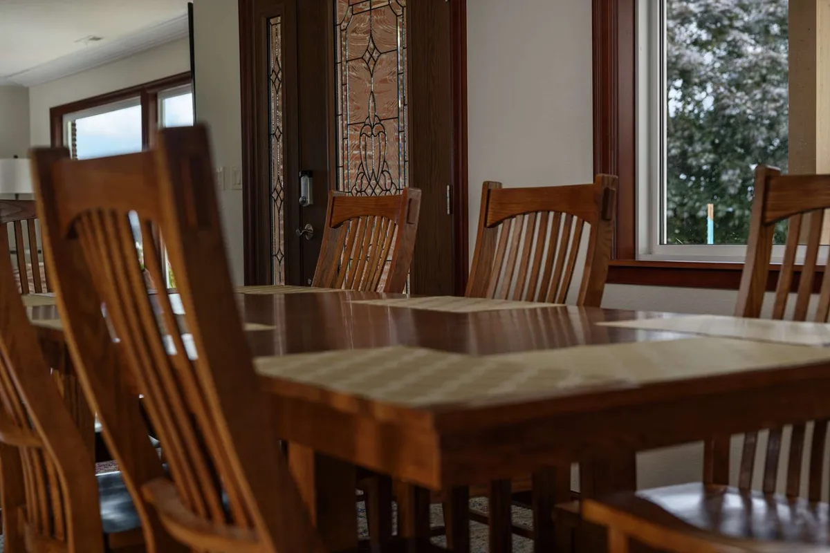 A warmly lit dining area centered around a wooden table, surrounded by comfortable dining chairs. The stained glass door adds a decorative touch, while the setup suggests a space perfect for small gatherings, celebrations, or shared meals. The room feels inviting and intimate, ideal for hosting memorable moments with close friends or family.