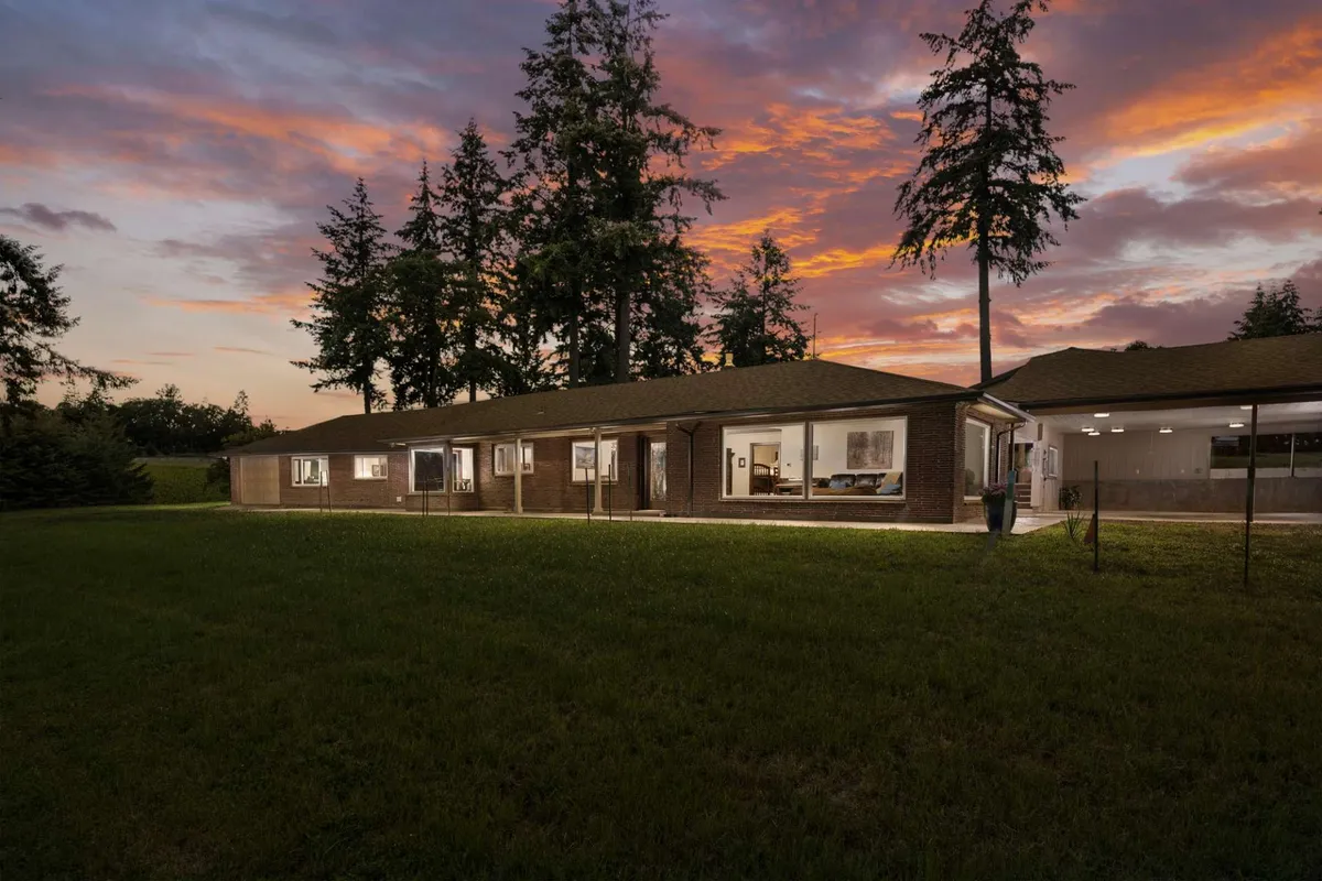 This exterior image captures the Blanchard Homestead under a serene sunset sky, surrounded by mature trees and open green space. The house is welcoming, with hints of an expansive yard perfect for outdoor family gatherings and relaxation after a day spent exploring the region.