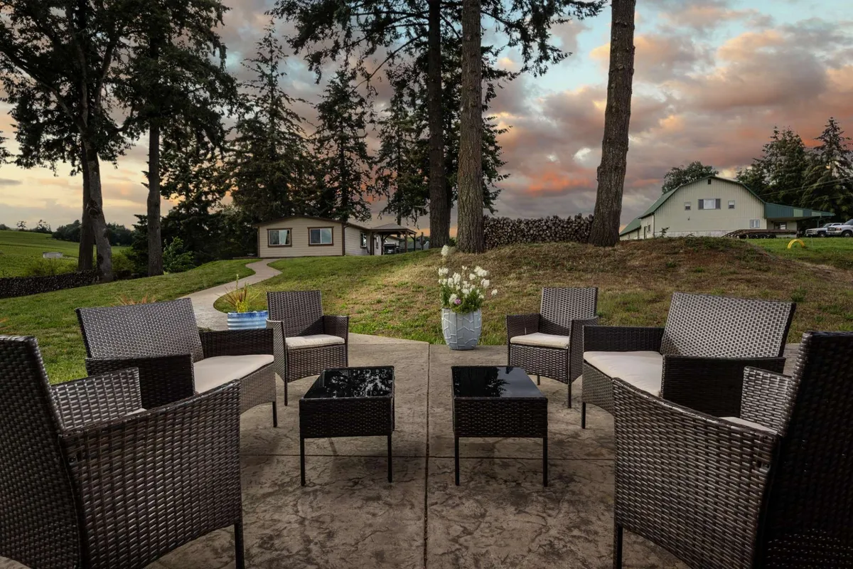 A welcoming outdoor seating area features comfortable chairs and a flower pot along a paved garden path. The warm, tranquil setting invites evening conversations, stargazing, or quiet reflection, all set against the backdrop of a beautiful sunset glow.