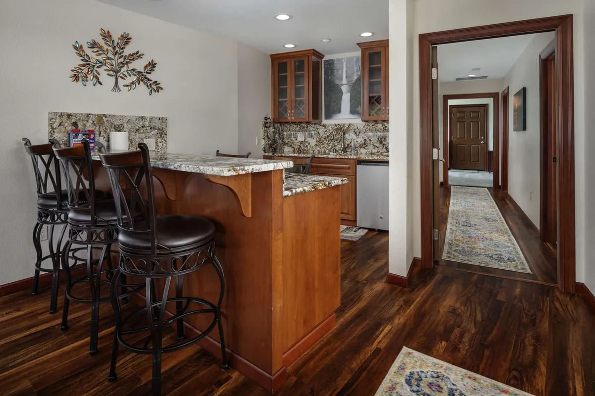 A welcoming kitchen setting with a large granite countertop, bar stools for casual seating, decorative wall art, and warm wood cabinetry. The space feels ideal for both food preparation and hosting informal meals or drinks.