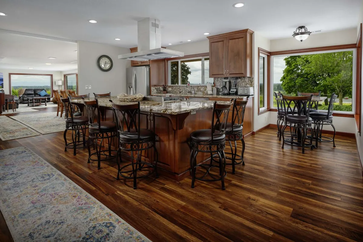 The hero image showcases a beautifully updated kitchen with a striking granite island, surrounded by warm wooden cabinetry and expansive windows that frame sweeping vineyard views. The space is filled with natural light, inviting gatherings for morning coffee or festive meals while enjoying the serene landscape of Oregon wine country.