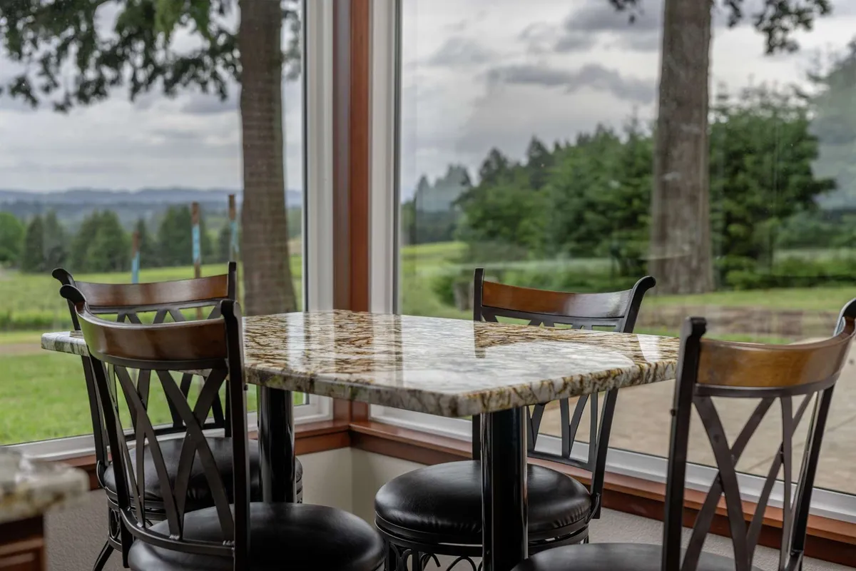 A relaxed dining area with a granite table, wooden chairs, and large windows that offer scenic views. The setup is perfect for casual dining, coffee chats, or enjoying meals with a view of the outdoors.