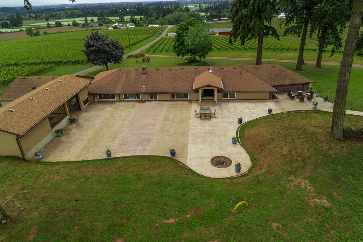 An exterior shot featuring the house, outdoor seating area, nearby vineyards, and a glowing fire pit, suggesting possibilities for outdoor dining, relaxing, and social gatherings as the sun sets.