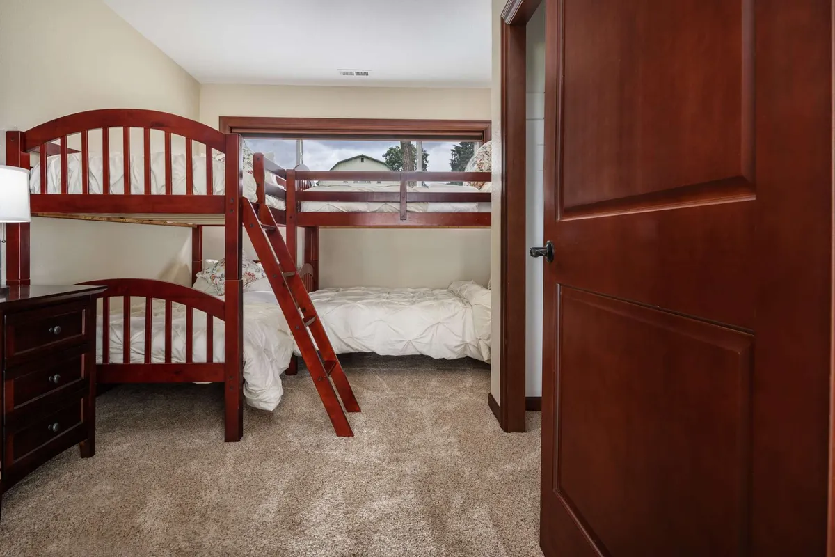 A playful yet restful bunk room with built-in bunk beds, a nightstand with a lamp, and a doorway leading to the rest of the home. The space is designed to be both fun and comfortable for younger guests or groups of friends.